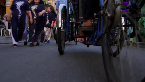 Traditional-Vietnamese-cycle-rickshaw's-wheels-carrying-tourist-in-narrow-road-of-old-town-in-Hoi-An-city,-Vietnam,-Low-angle-shot