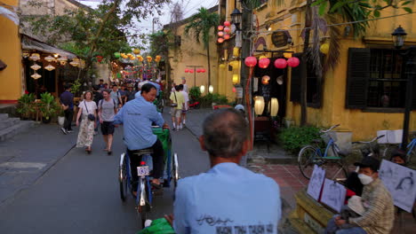 Traditionelle-Vietnamesische-Fahrradrikschas,-Die-Touristen-In-Der-Engen-Straße-Der-Altstadt-Von-Hoi-An-Befördern,-Während-Andere-Touristen-Einen-Rundgang-Machen,-Vietnam
