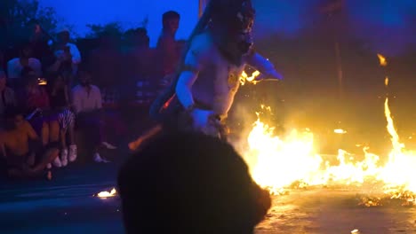 Handheld-shot-of-Balinese-cultural-fire-dance-of-characters-kicking-flames-during-nightfall