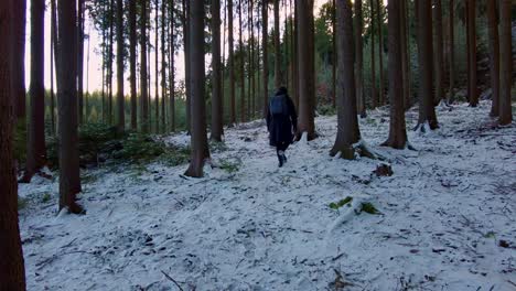 Traveler-in-a-black-jacket-with-a-backpack-walks-through-a-snowy-forest-in-winter