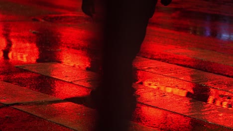 Rotes-Licht-Reflektiert-Auf-Nasser-Straße,-Während-Eine-Person-In-Zeitlupe-Die-Straße-überquert