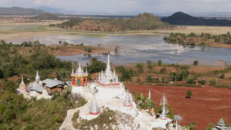 Cinematic-drone-shot-of-Taw-Kyet-Mountain-Pagoda-surrounded-by-flooded-fields-in-Myanmar