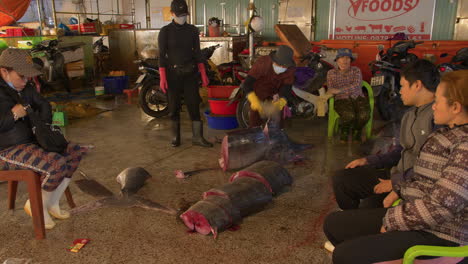Woman-cutting-big-dog-salmon-on-the-floor-and-other-people-watching-at-Tho-Quang-fishing-port,-Vietnam