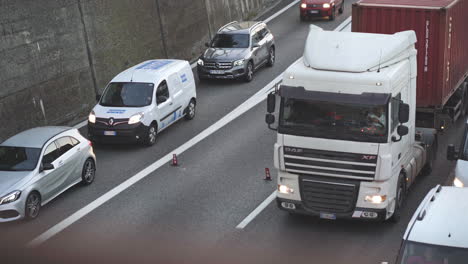 Telephoto-shot-of-trucks-and-cars-driving-slow-caused-by-roadworks,-tilt-up