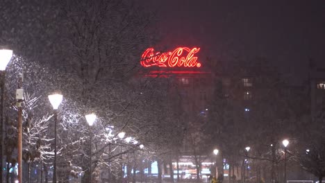 Snow-falls-on-glowing-red-Coca-Cola-sign-on-top-of-factory-with-well-lit-sidewalk