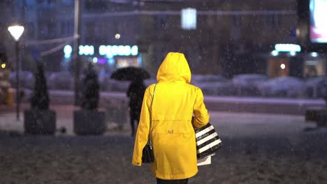 Person-in-yellow-rain-jacket-walks-away-in-slow-motion-as-snow-falls