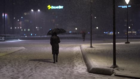Eine-Ganz-In-Schwarz-Gekleidete-Frau-Mit-Regenschirm-Geht-Weg,-Während-Schnee-Fällt