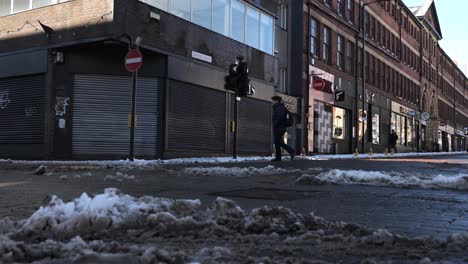 Bus-turning-down-street-as-man-crosses-snowy-road,-Sheffield,-low-angle