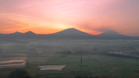 Aerial-view-of-rural-landscape-in-foggy-morning-with-view-of-mountain-range-and-sunrise-sky