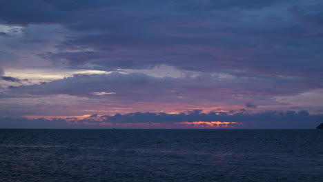 Brennender-Sonnenuntergangshimmel-Am-Meer-Mit-Violett-rosa-orangefarbenem-Sonnenschein,-Der-Sich-In-Tief-Schwebenden,-Dichten,-Flauschigen-Wolken-Widerspiegelt
