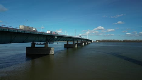 Drohne-Fliegt-über-Einen-Fluss-Neben-Einer-Blauen-Brücke-Mit-Einer-Nationalstraße