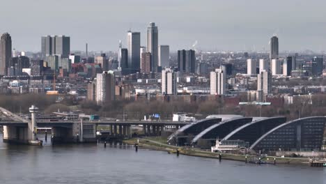 Wide-aerial-panning-shot-of-the-Rotterdam-skyline-with-the-Van-Brienenoord-bridge-over-the-Nieuwe-Maas,-and-vehicle-traffic