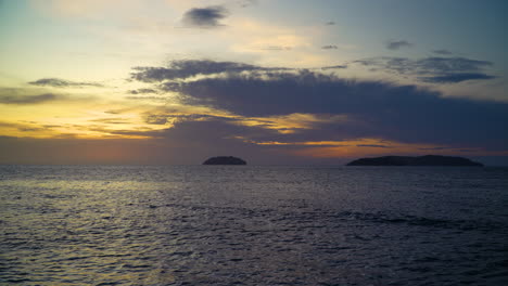 Goldener-Sonnenuntergang-über-Dem-Meer,-Sonnenlicht-Spiegelt-Sich-In-Der-Ruhigen-Wasseroberfläche,-Silhouette-Von-Inseln-Im-Hintergrund,-Dramatischer-Himmel-Am-Meeresstrand