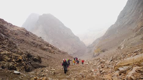 "A-group-of-climbers-slowly-ascends-a-rocky-mountain,-using-trekking-poles-for-support