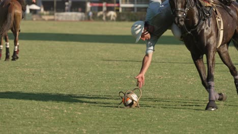 Sport-motion-shot-capturing-a-man-attempting-to-pick-up-the-horseball-on-the-field-while-riding-on-the-back-of-galloping-horse,-following-the-rule-of-the-game,-during-pato-match,-Buenos-Aires