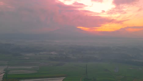 Hyperlapse-aerial-footage-of-rice-field-with-mountain-range-and-cloudy-sunrise-sky