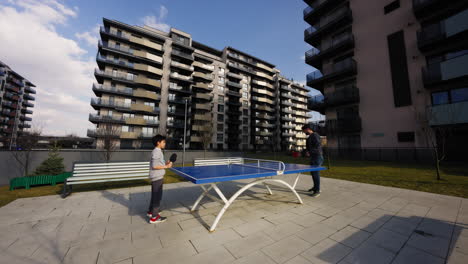 Dos-Personas-Jugando-Tenis-De-Mesa-Afuera,-En-Un-Parque-Residencial-De-Lujo,-En-Un-Día-Soleado