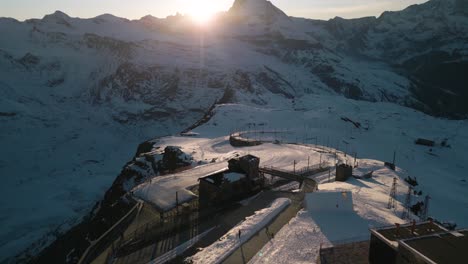 Drone-Flies-Over-Gornergrat,-Pan-Up-to-Reveal-Matterhorn-at-Sunset