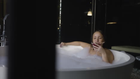 Slow-motion-shot-of-an-attractive-female-relaxing-in-a-soapy-bath-drinking-a-cocktail