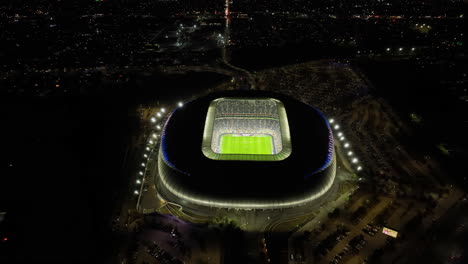 Drone-shot-tilting-over-the-night-lit-BBVA-stadium,-in-Monterrey-city,-Mexico
