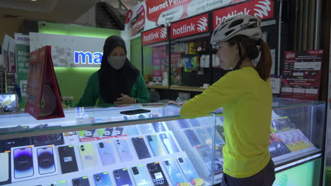 Un-Ciclista-Espera-Pacientemente-En-Un-Centro-Comercial-Mientras-Un-Especialista-En-Telefonía-Cambia-Las-Tarjetas-SIM