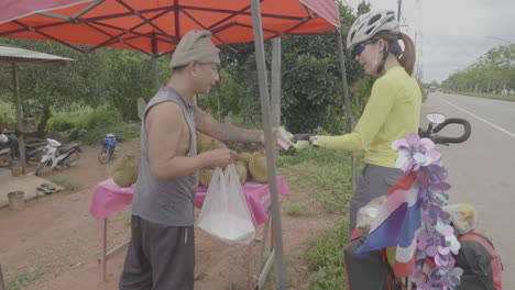 Woman-cyclist-buys-fruit-and-pays-roadside-vendor-in-southeast-asia