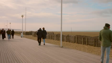 Shot-of-people-passing-by-along-the-seaside-in-Promenade-des-Anglais,-Deauville,-France-on-a-cold-winter-evening