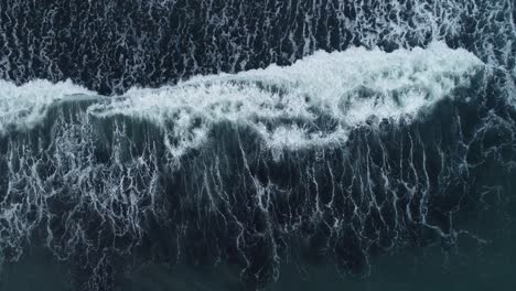 Birds-eye-drone-footage-of-waves-breaking-over-a-black-sand-beach-in-Iceland