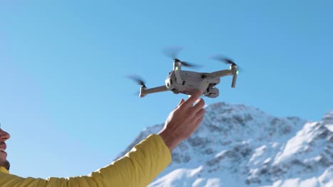 Drone-lands-into-caucasian-man-hand-with-snow-covered-mountains-in-the-background-on-a-sunny-winter-day