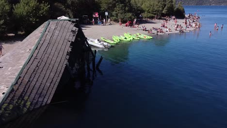 Aerial-shot-of-tourist-swimming-on-the-beach-in-the-lake-surrounded-by-forest-in-Bariloche,-Colonia-Suiza,-Patagonia-Argentina