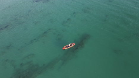 Aerial-view-of-lone-fisherman-in-orange-rowboat-shallow-sea-water
