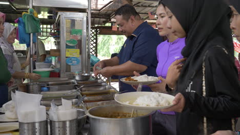 Travelers,-athletes,-and-locals-serve-food-onto-plates-of-rice-in-Malaysia