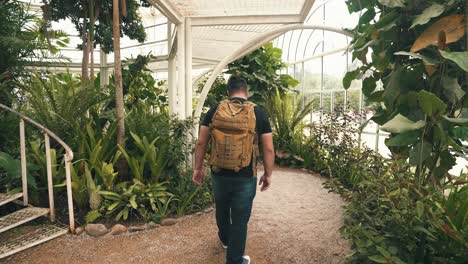 Young-male-traveler-with-backpack-walking-through-a-tropical-greenhouse-in-slow-motion
