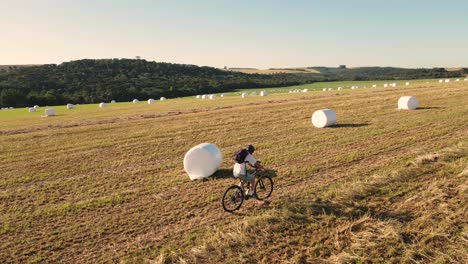 Cyclist-in-harvested-field-between-rolls-of-hay-silage,-aerial-drone-view