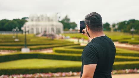Man-taking-a-picture-of-the-greenhouse-and-garden-with-cell-phone-of-Botanical-Garden,-Located-in-Curitiba,-Brazil