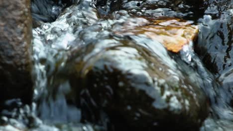 Zeitlupenaufnahme-Von-Wasser,-Das-In-Einem-Kleinen-Bach-über-Einige-Felsen-Fließt