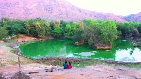 beautiful-couple-setting-on-rock,-mountain-in-the-middle-of-forest-area-and-river-view,-Drone-Camera-moving-backward-overhead-to-beautiful-couple,-couple-relaxing-on-naturel-beauty