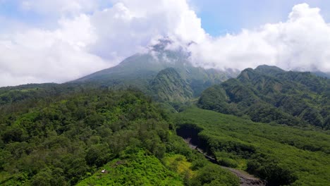 Aerial-push-out-shot-of-green-landscape-with-Merapi-Volcano-surrounded-by-white-clouds-in-Indonesia