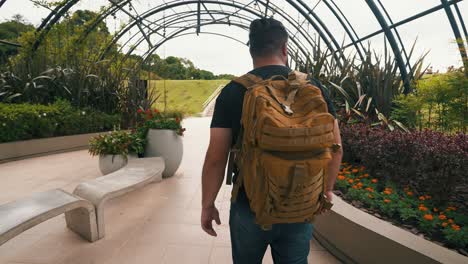 Young-male-traveler-with-backpack-walks-through-a-tropical-greenhouse-handheld-shot