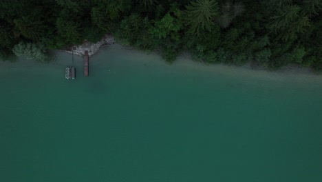Top-down-aerial-shot-at-a-pier-in-a-turquoise-lake-with-green-treetops-at-the-shore,-beautiful-landscape
