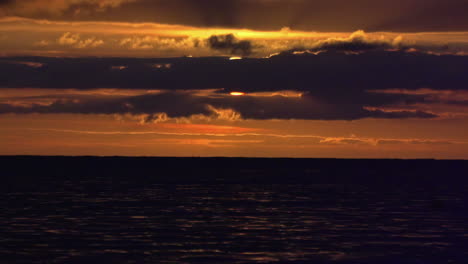 Shot-over-the-water-and-the-orange-horizon-and-the-sun-hidden-by-the-clouds