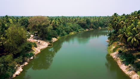 Kerala-landscape-with-river-and-coconut-trees-around-its-blue-evening-sky,-aerial-camera-moving-forward-to-palm-forest-and-lake-view