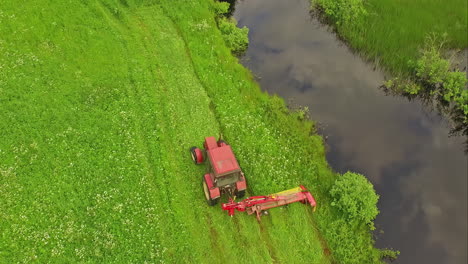 Tractor-with-side-mower-cutting-grass-along-canal-shore-on-green-field