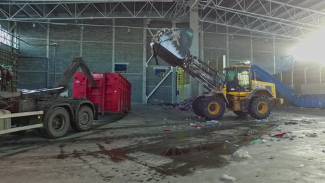 Excavator-loading-trash-into-container-in-recycling-yard-during-sunny-day,-slow-motion