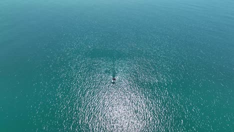 Birdseye-view-of-lone-boat-drifting-in-open-ocean-on-glistening-water