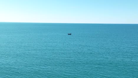 Single-boat-floats-in-open-ocean-on-blue-sunny-day-aerial-dolly