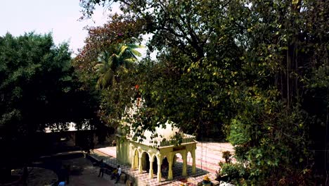 The-aerial-camera-moves-backward-and-zooms-out-on-the-scene,-Indian-temple-and-big-trees-in-the-foreground-of-the-temple