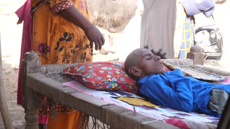 Niño-Paquistaní-Discapacitado-Acostado-En-La-Cama-Afuera-En-Sindh-Con-Su-Familia-A-Su-Lado