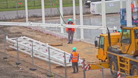 Two-workers-dressed-in-orange-overalls,-on-a-crane-in-a-building-under-construction