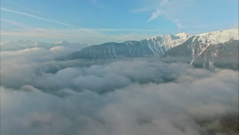 Drone-flying-over-clouds-with-snowy-mountains-in-background